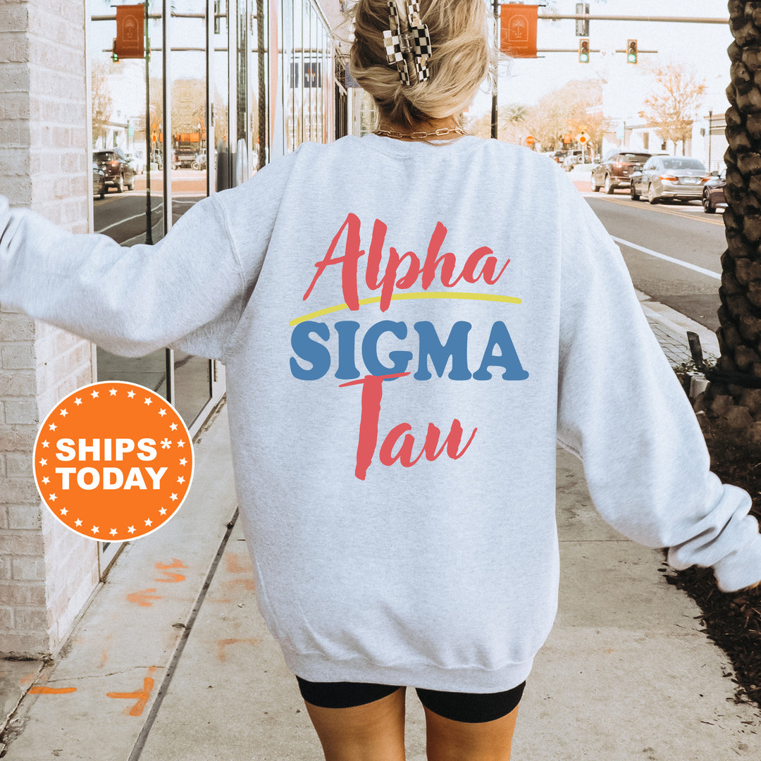 A woman wearing a grey sweatshirt with the text "Alpha Sigma Tan" printed on it, standing on a sidewalk with a traffic light in the background.