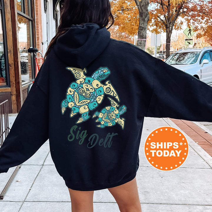 A person wearing a black hoodie with a colorful turtle design and the text "Sign Delt" printed on it, standing on a sidewalk with a car and a building in the background.