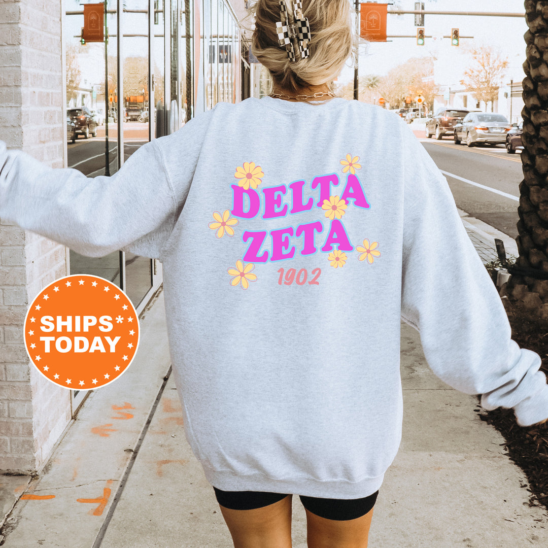 A person wearing a gray sweatshirt with the text "DELTA ZETA" and "1902" printed on it, standing on a sidewalk with a brick building in the background.