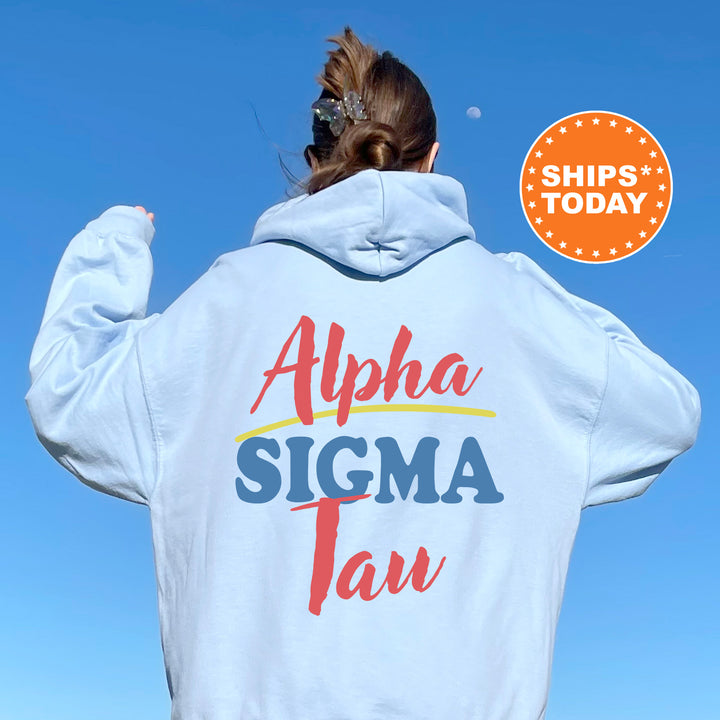 A person wearing a white hoodie with the text "Alpha Sigma Tau" printed on it, standing against a clear blue sky.