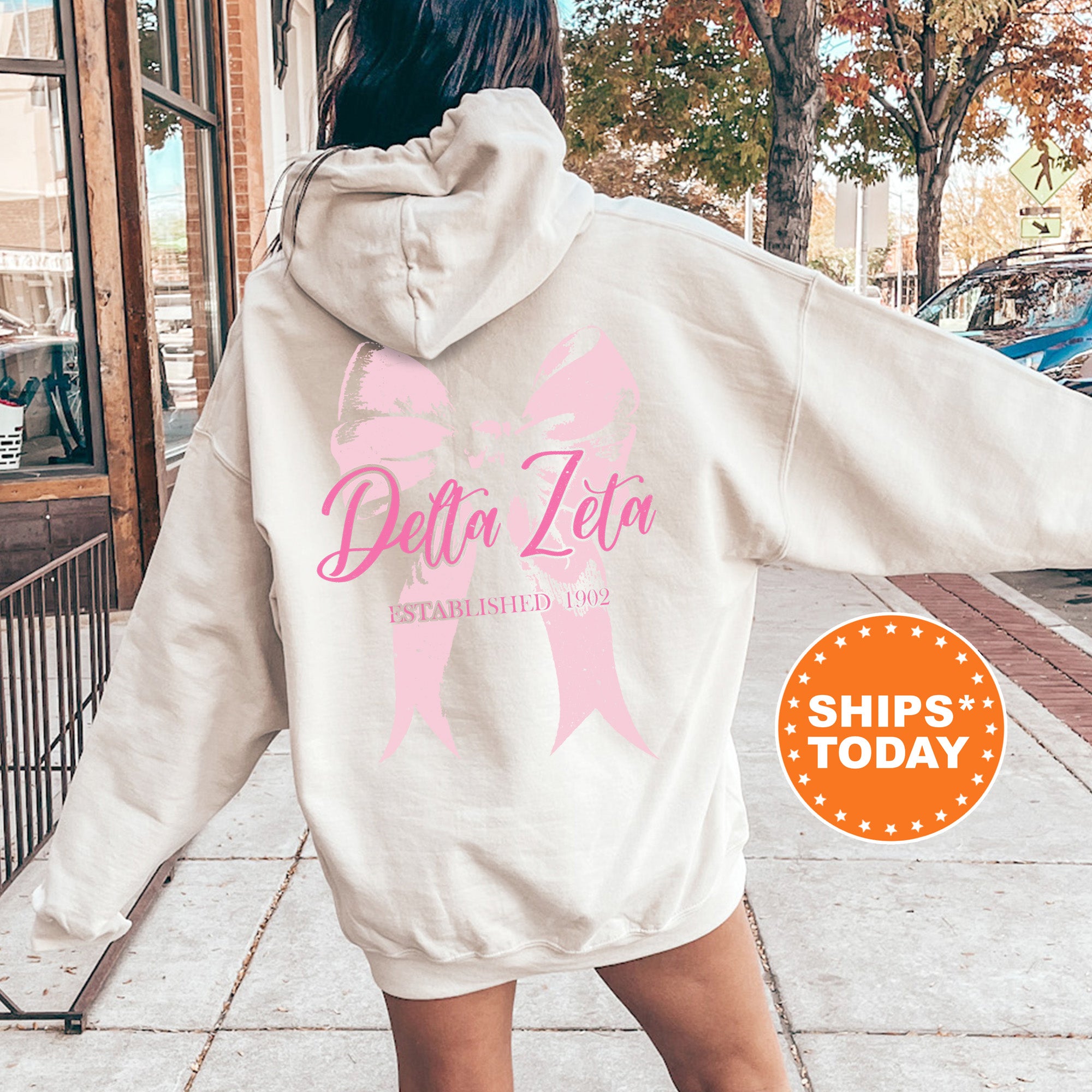 a woman walking down a sidewalk with a pink ribbon on her hoodie