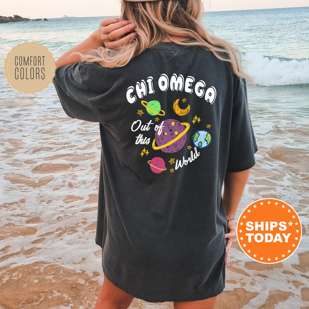 A woman wearing a black t-shirt with a colorful graphic design of planets and stars on the back, standing on a beach with the ocean in the background.