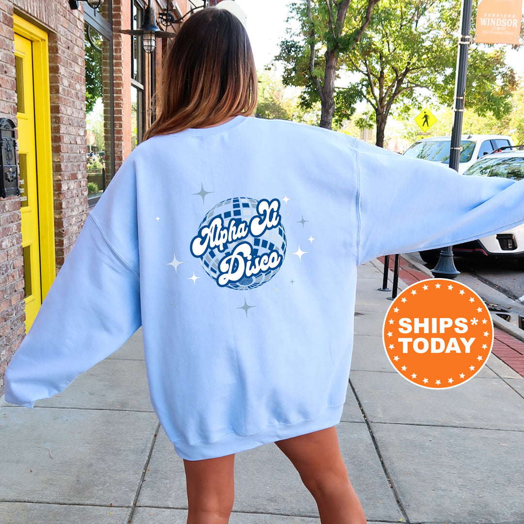 A woman wearing a light blue sweatshirt with a graphic design on the back, standing on a sidewalk.