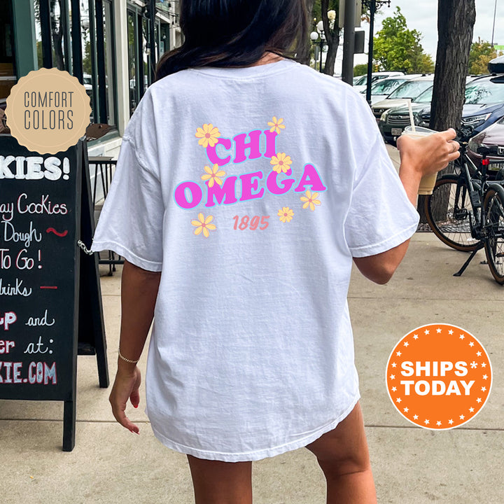 A person wearing a white t-shirt with the text "CHI OMEGA" printed on it, standing on a sidewalk next to a chalkboard sign.