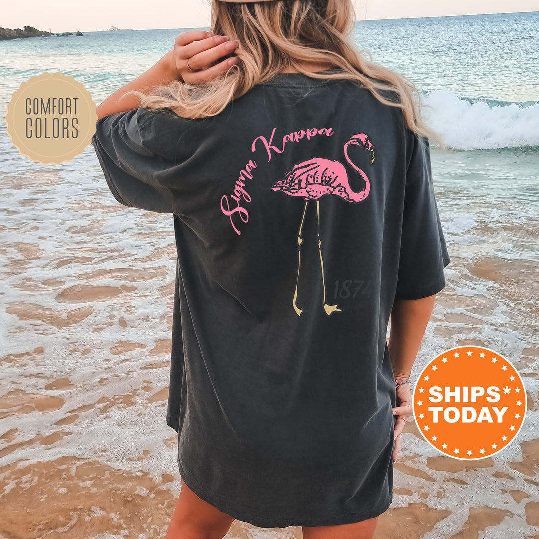 a woman standing on a beach wearing a black shirt with a pink flamingo on