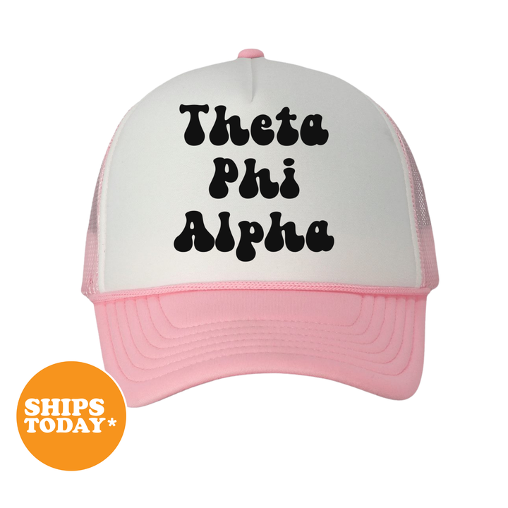 A white and pink baseball cap with the text "Theta Phi Alpha" printed on it.