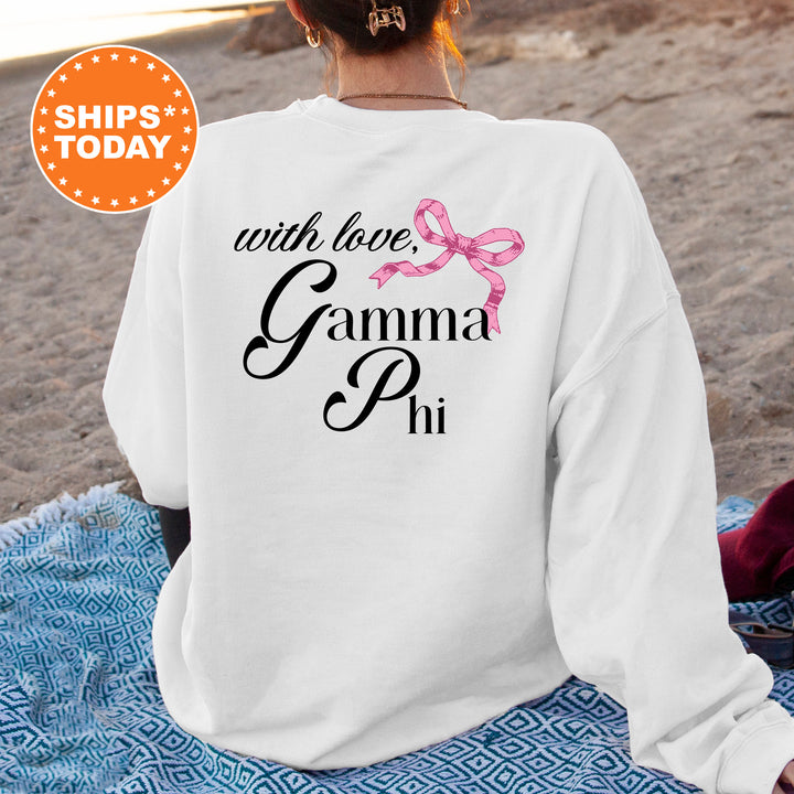 a woman sitting on the beach wearing a white sweatshirt with a pink ribbon