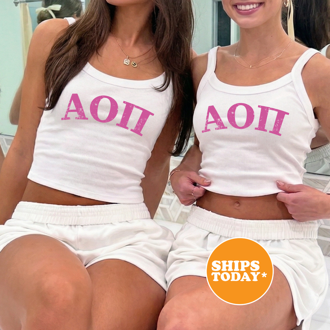 Two women wearing matching white tank tops with the letters "AOI" printed on them, posing together in front of a mirror.