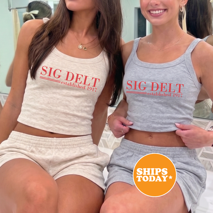 Two women wearing matching gray tank tops with the text "SIG DELT established 1917" are posing together in front of a mirror.