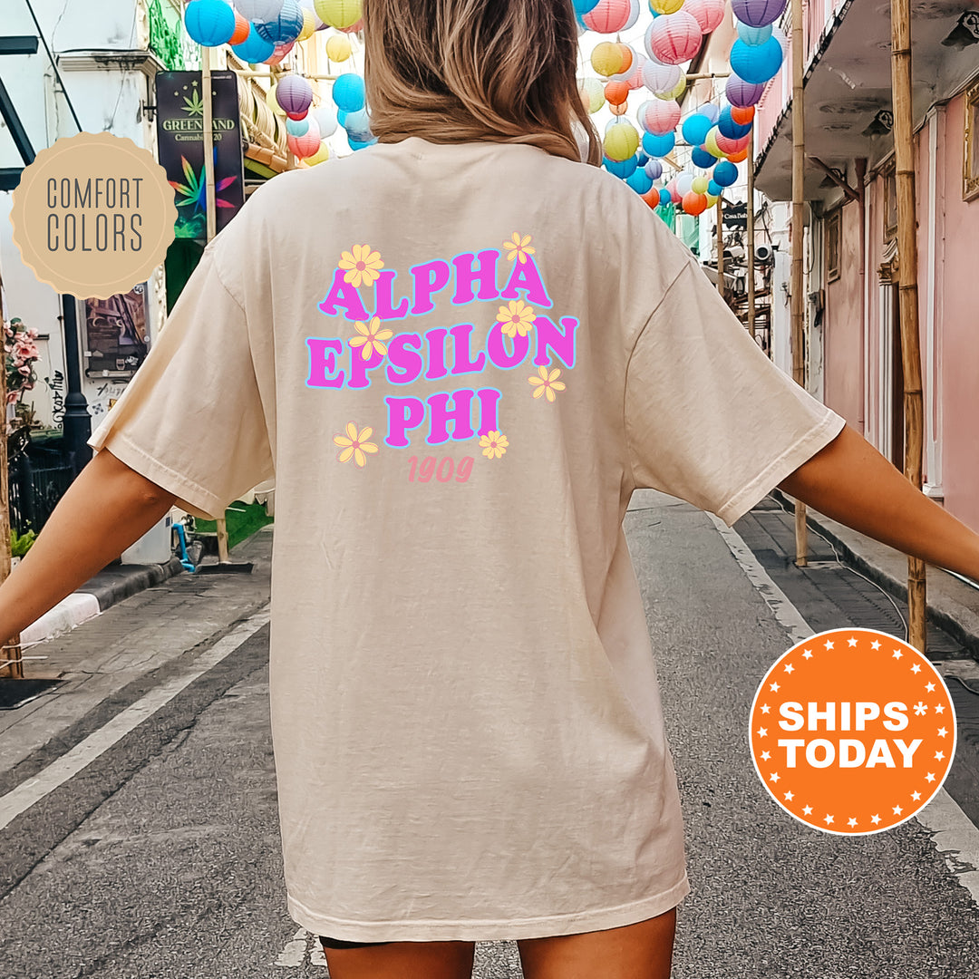 A person wearing a beige t-shirt with the text "ALPHA EPSILON PHI" printed on it, standing in front of a street lined with colorful lanterns.