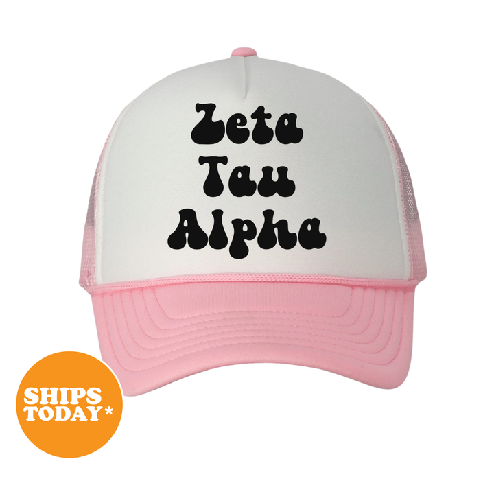 A pink and white baseball cap with the text "Zeta Tau Alpha" printed on it.