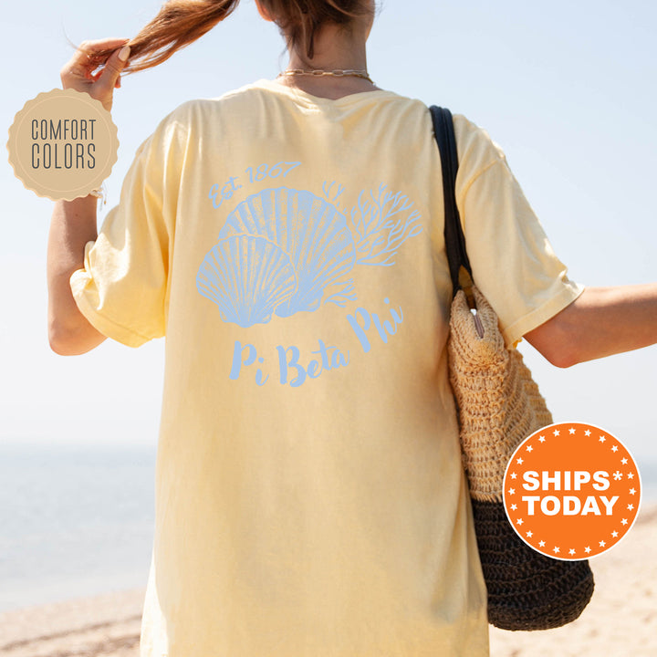 A person wearing a yellow t-shirt with a blue design and text, standing on a beach with a handbag and a sign advertising "SHIPS TODAY".