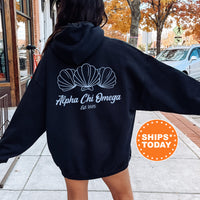 A person wearing a black hoodie with the logo of Alpha Chi Omega sorority, which is a sorority with a focus on women's leadership and community service.