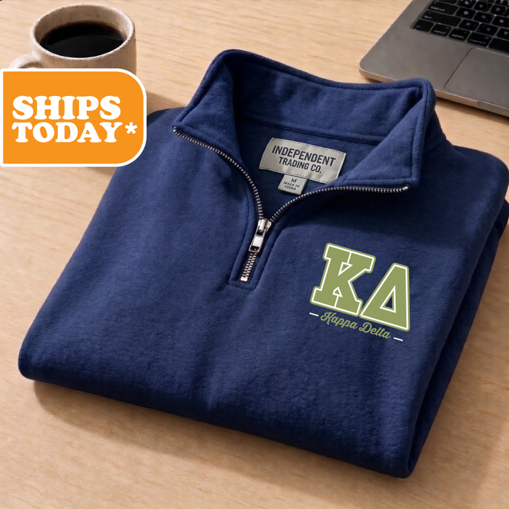 A navy blue zip-up jacket with a logo for Kappa Delta sorority is displayed on a wooden surface, accompanied by a laptop and a coffee cup.