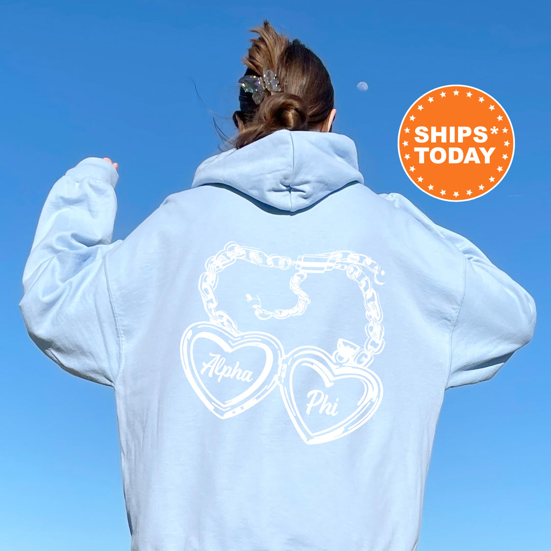 A person wearing a light blue hoodie with a heart-shaped charm and the text "Alpha Phi" printed on the back.