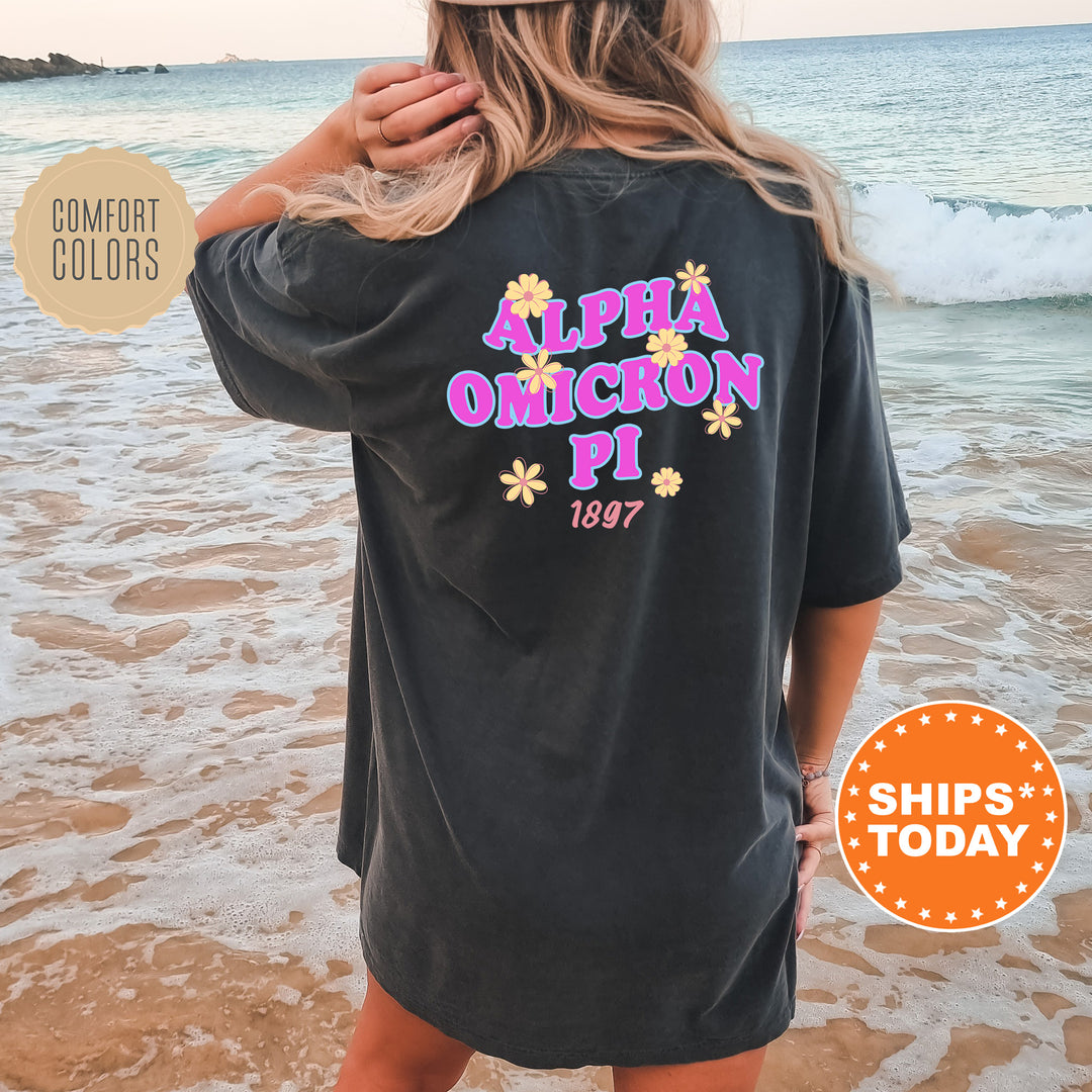 A woman wearing a black t-shirt with text and graphics printed on it, standing on a beach with waves in the background.