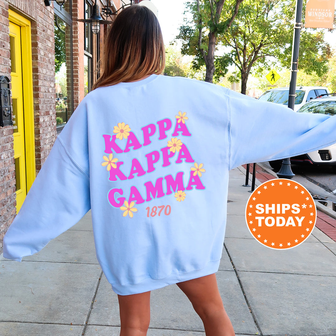 A woman wearing a light blue sweatshirt with the text " Kappa Kappa Gamma" printed on it, standing on a sidewalk.