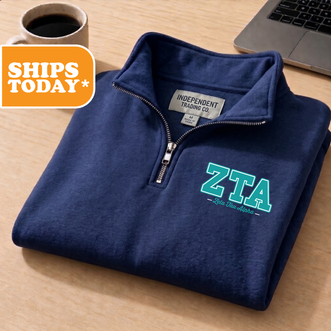A navy blue zip-up jacket with the text "ZTA" printed on the front, placed on a wooden surface next to a laptop and a coffee cup.
