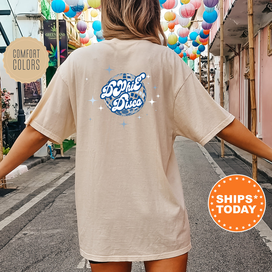 A person wearing a beige t-shirt with a graphic design on the back, standing on a street with colorful lanterns hanging overhead.