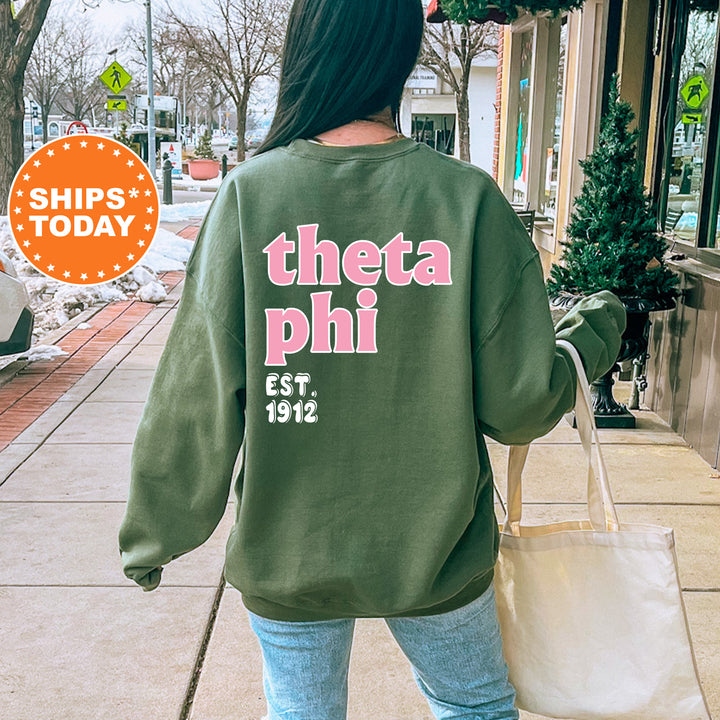 A person wearing a green sweatshirt with the text "theta phi EST. 1912" printed on it, walking on a sidewalk.