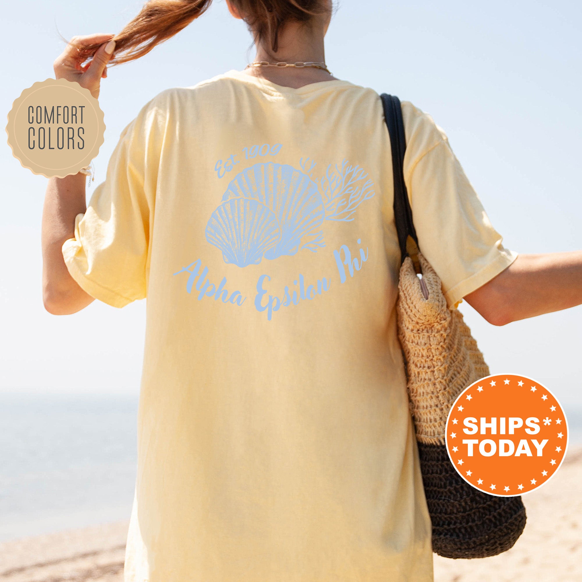 A person wearing a yellow t-shirt with a blue design and text, standing on a beach with a handbag and a sign advertising 