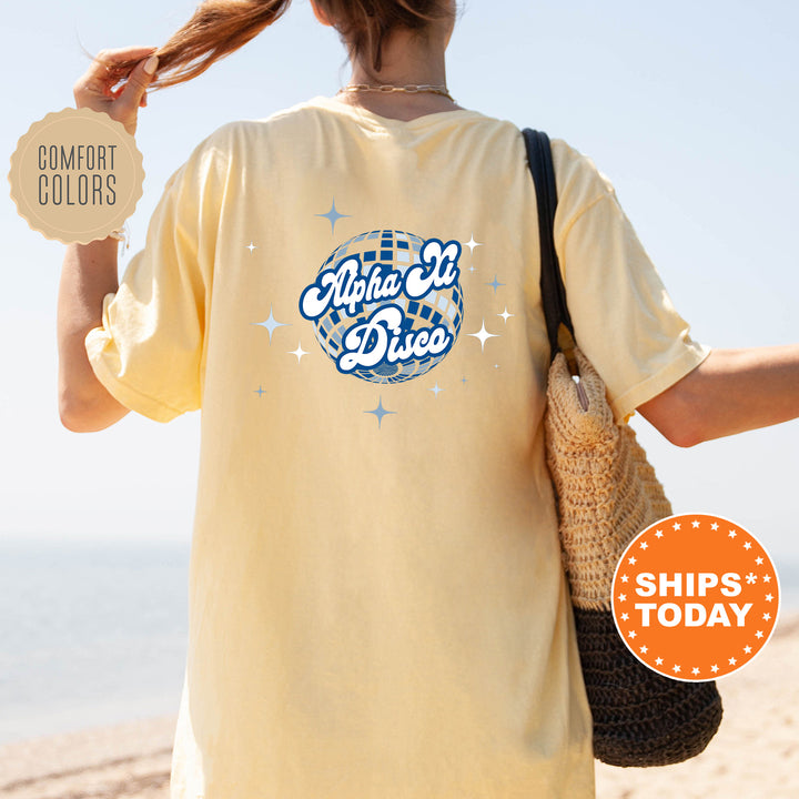 A person wearing a yellow t-shirt with a graphic design and text, standing on a beach with a handbag.