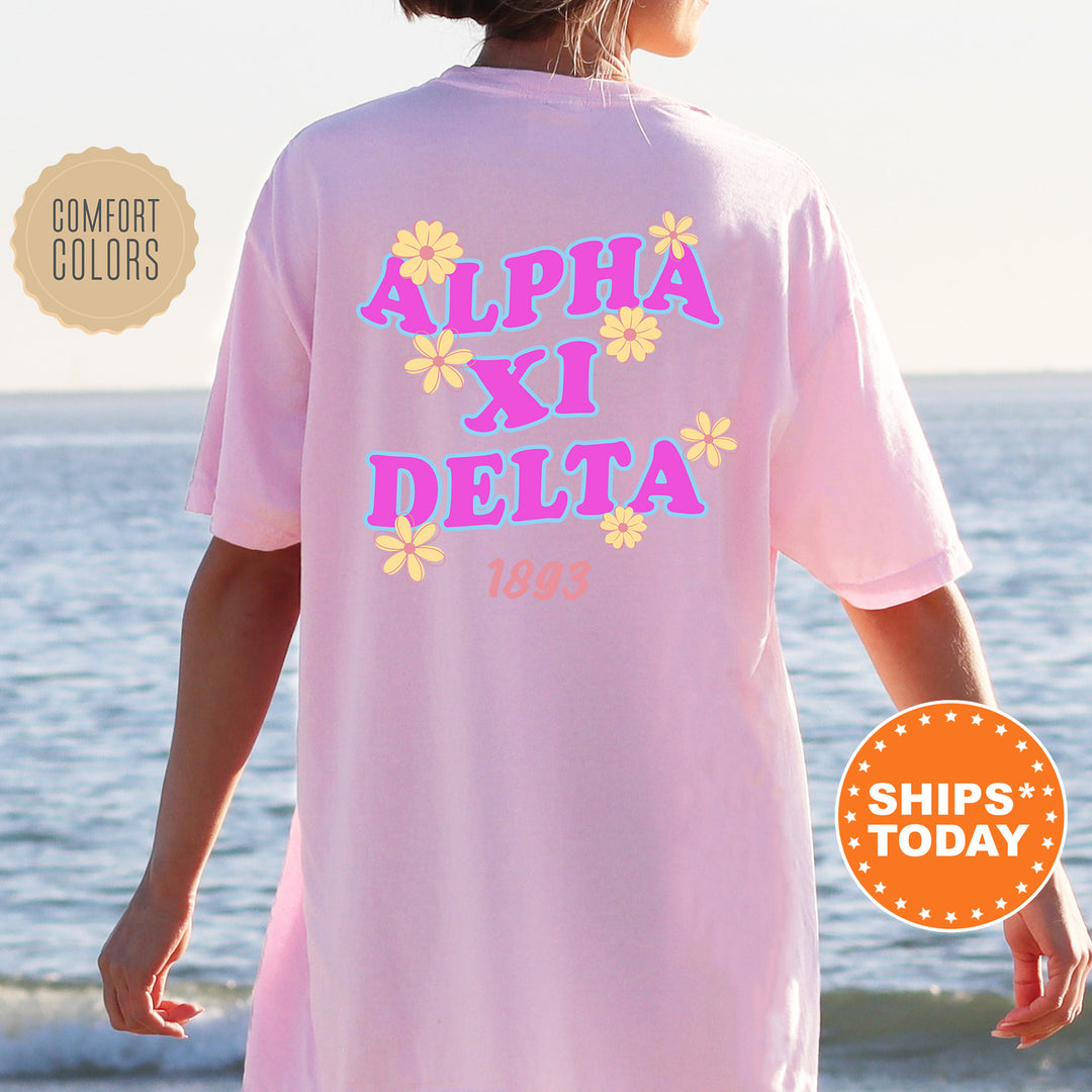 A person wearing a pink t-shirt with the text "ALPHA XI DELTA" printed on it, standing near the ocean.