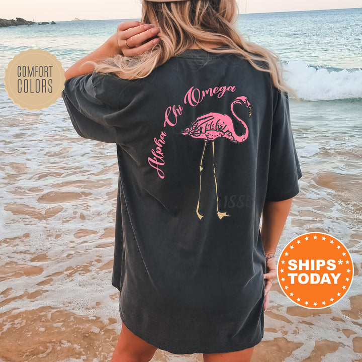 a woman standing on a beach wearing a black shirt with a pink flamingo on