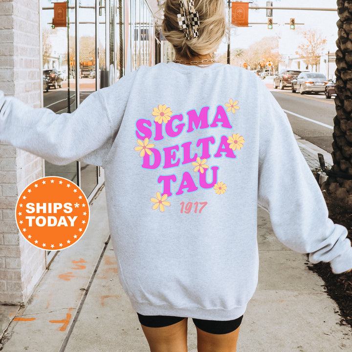 A person wearing a gray sweatshirt with the text "SIGMA DELTA TAU" printed on it, standing on a sidewalk.
