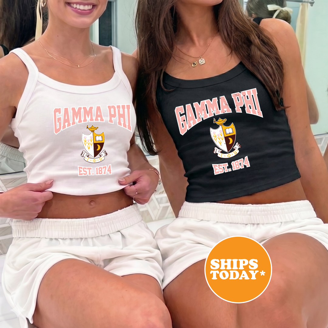 Two women wearing matching white tank tops with the text "Gamma Phi" and "Gamma Phi Est. 1974" printed on them, along with a shield emblem.