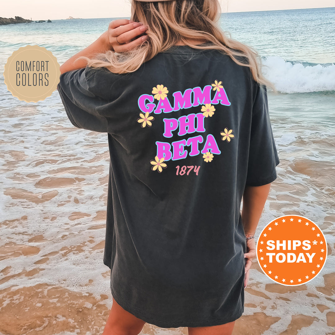 A woman wearing a black t-shirt with the text "GAMMA PHI BETA" printed on it, standing on a beach with the ocean in the background.