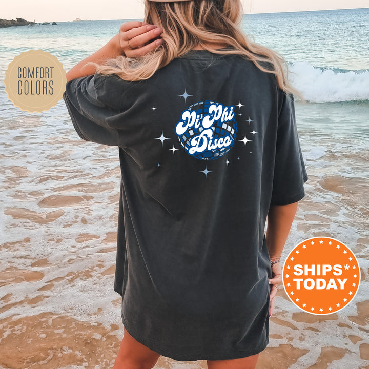 A woman wearing a black t-shirt with a graphic design on the back is standing on a beach, with the ocean and waves visible in the background.