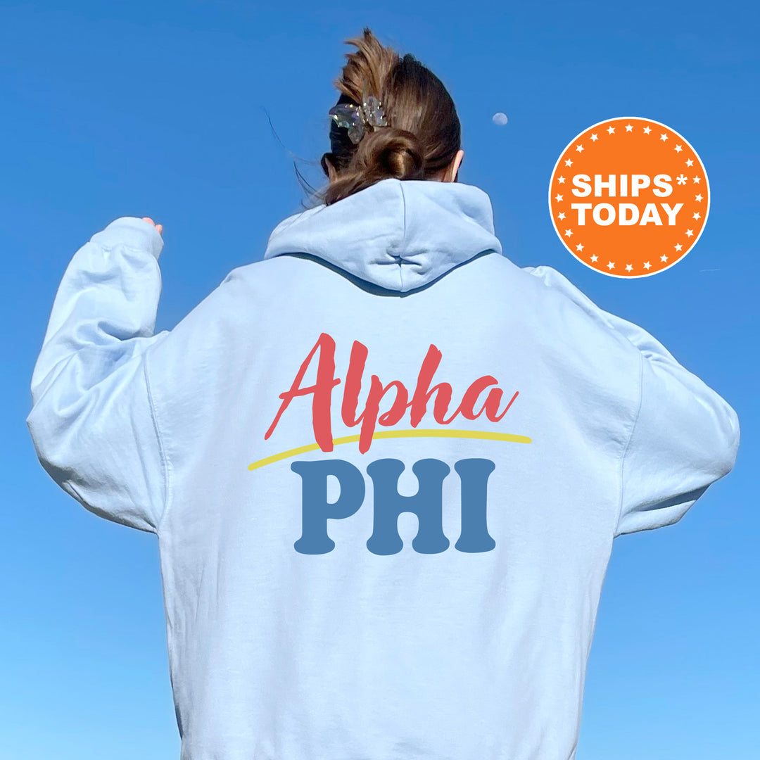 A person wearing a white hoodie with the text "Alpha Phi" printed on it, standing against a clear blue sky.