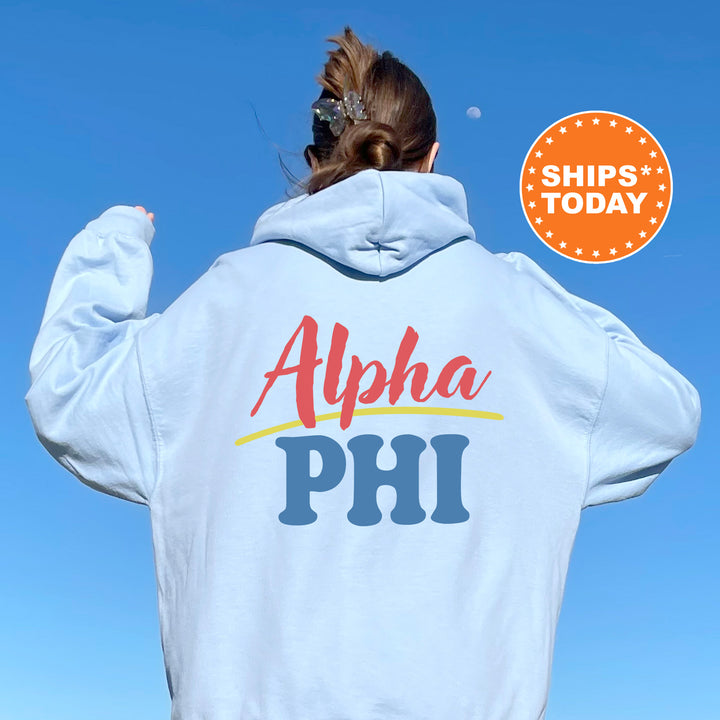 A person wearing a white hoodie with the text "Alpha Phi" printed on it, standing against a clear blue sky.