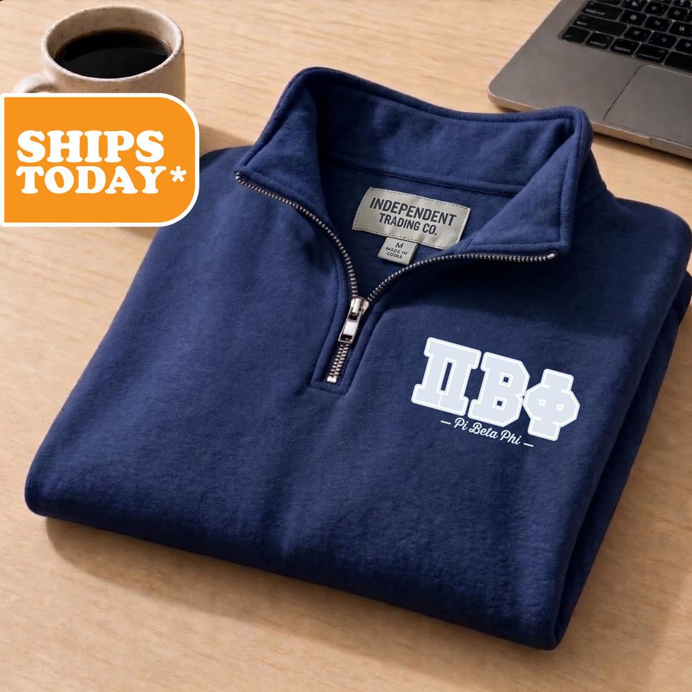 A navy blue zip-up jacket with a white logo on the front, placed on a wooden surface next to a laptop and a coffee cup.