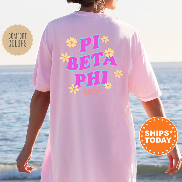 A person wearing a pink t-shirt with the text "PI BETA PHI 1867" printed on it, standing near the ocean.