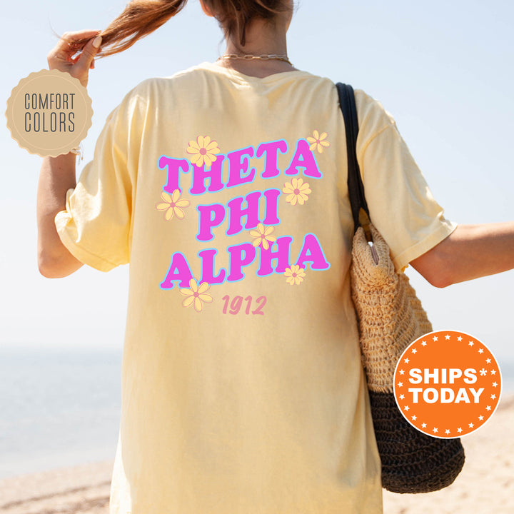 A person wearing a yellow t-shirt with the text "THETA PHI ALPHA 1912" printed on it, standing on a beach.