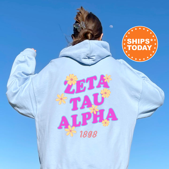 A person wearing a white hoodie with the text "ZETA TAU ALPHA 1898" printed on it, standing against a clear blue sky.