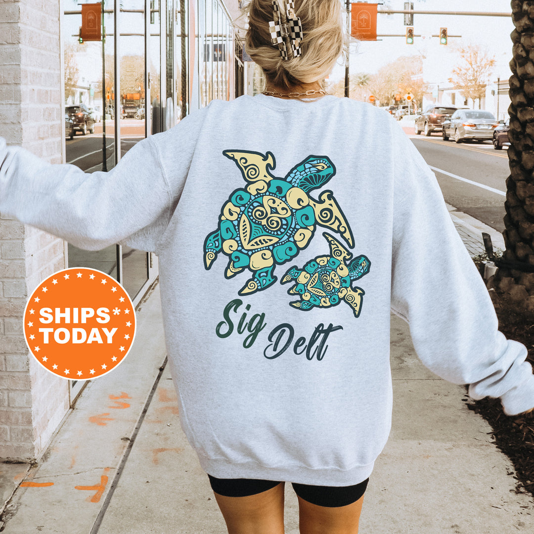 A person wearing a grey sweatshirt with a colorful turtle design and the text "Sig Delta" printed on it, standing on a sidewalk.