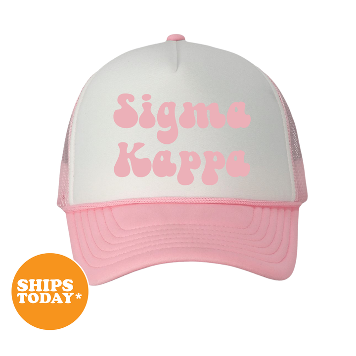 A pink and white baseball cap with the text "Signa Kappa" printed on it.