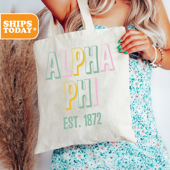 a woman holding a tote bag with the words alpha phi phi on it