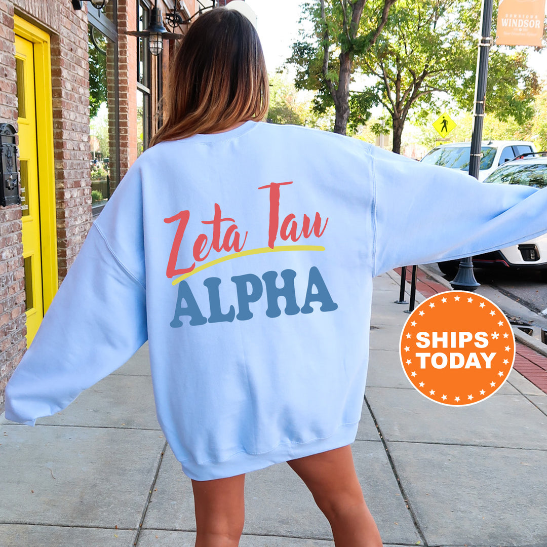 A woman wearing a light blue sweatshirt with the text "Zeta Tan" and "ALPA" printed on it, standing on a sidewalk.