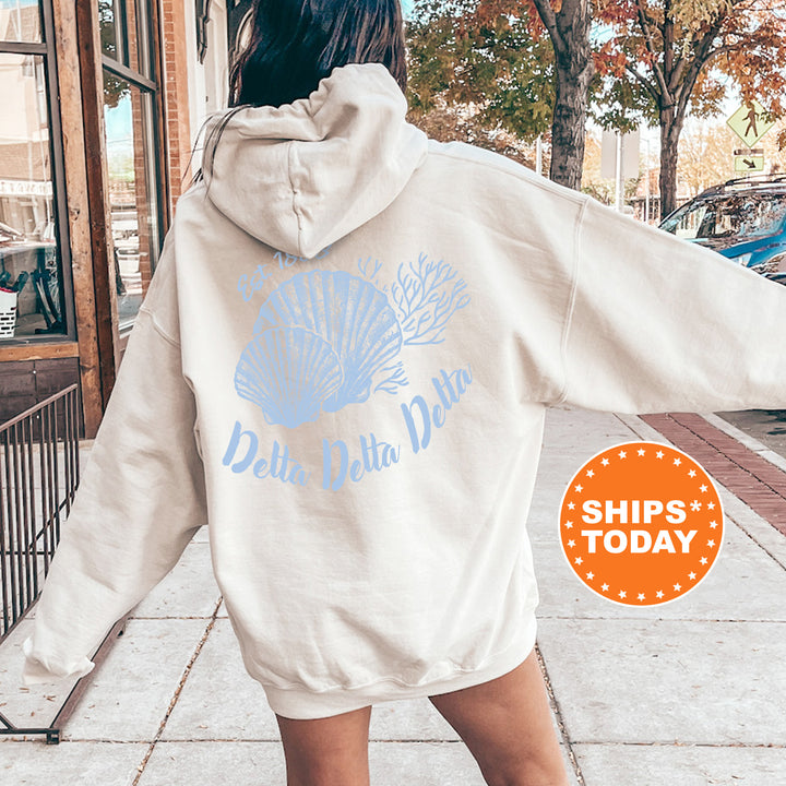 A person wearing a white hoodie with a blue graphic and text on the back is standing on a sidewalk.