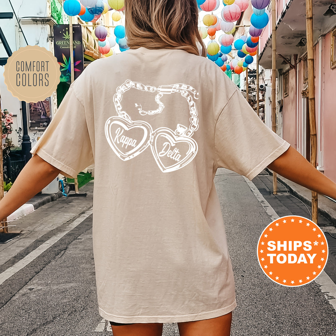 A woman wearing a beige t-shirt with a graphic design on the back, standing on a street with colorful lanterns hanging overhead.