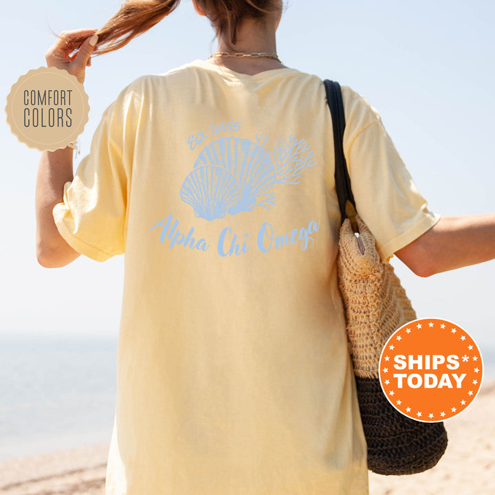 A person wearing a yellow t-shirt with a blue design and text, standing on a beach with a handbag and a sign advertising "SHIPS TODAY".