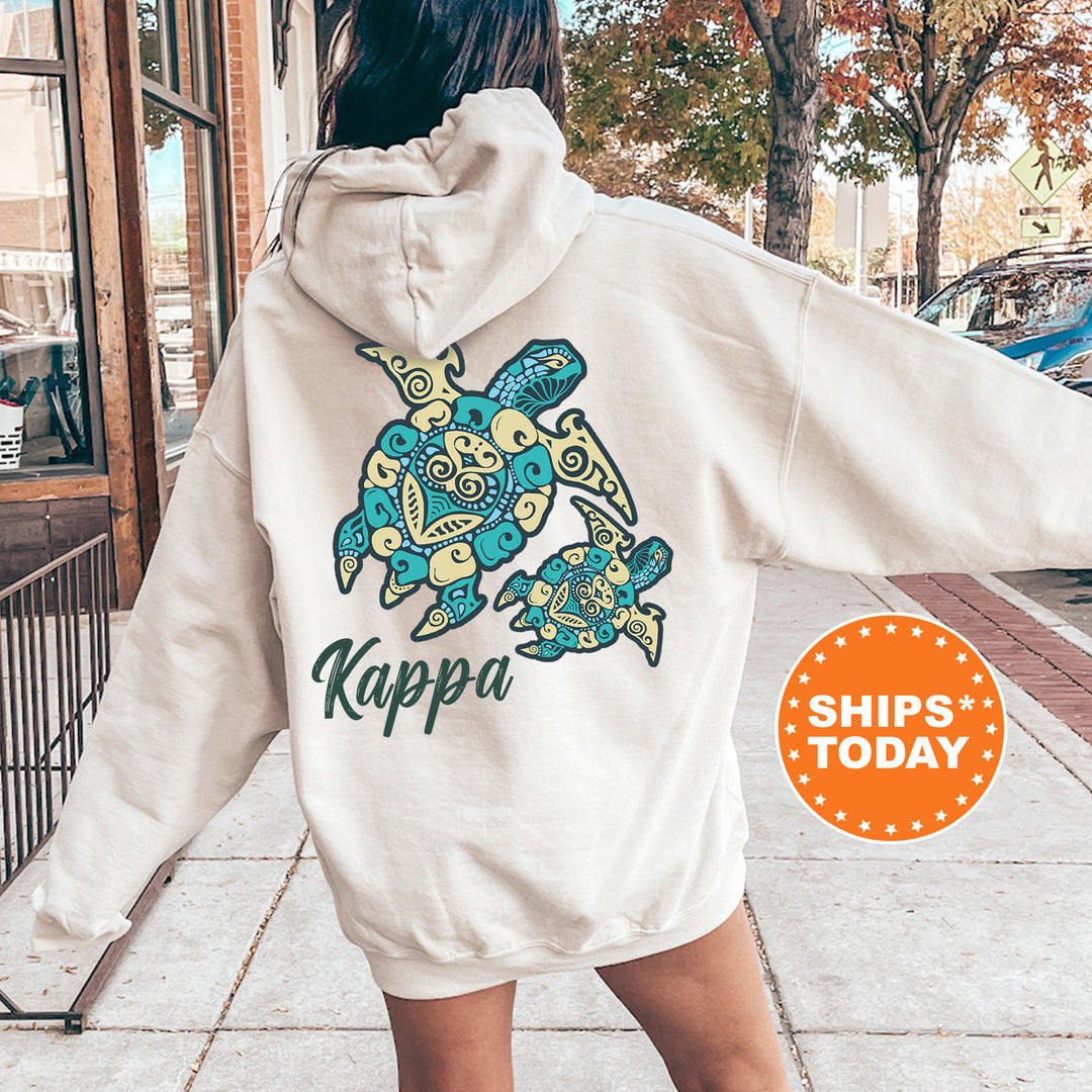 A person wearing a white hoodie with a colorful turtle design and the word "Kappa" printed on it, standing on a sidewalk.