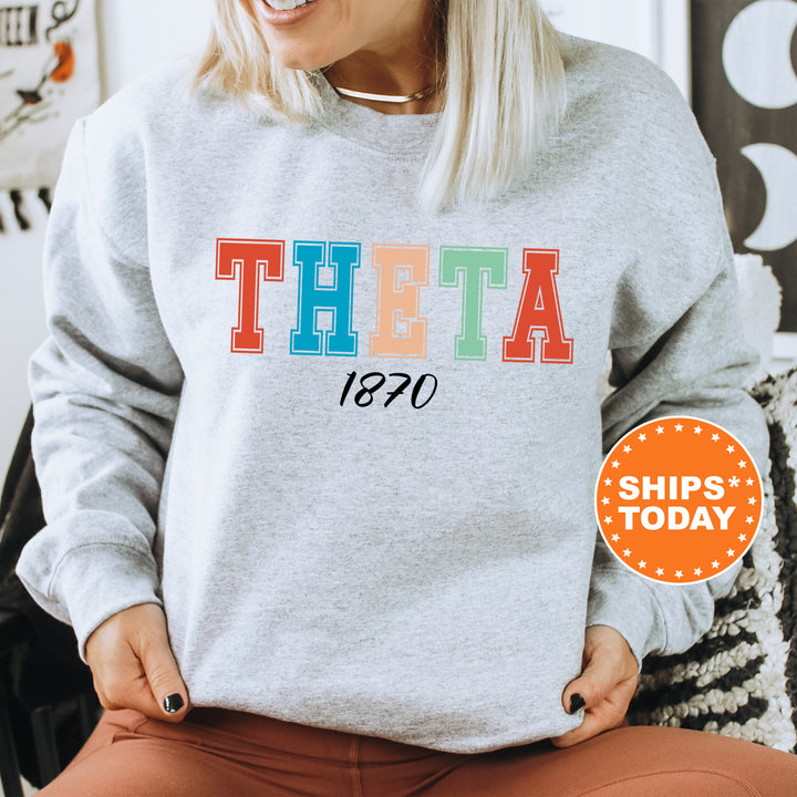 a woman sitting in a chair wearing a sweatshirt with the word theta printed on