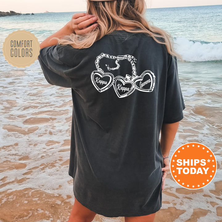 A woman wearing a black t-shirt with a graphic design on the back is standing on a beach, with the ocean visible in the background.