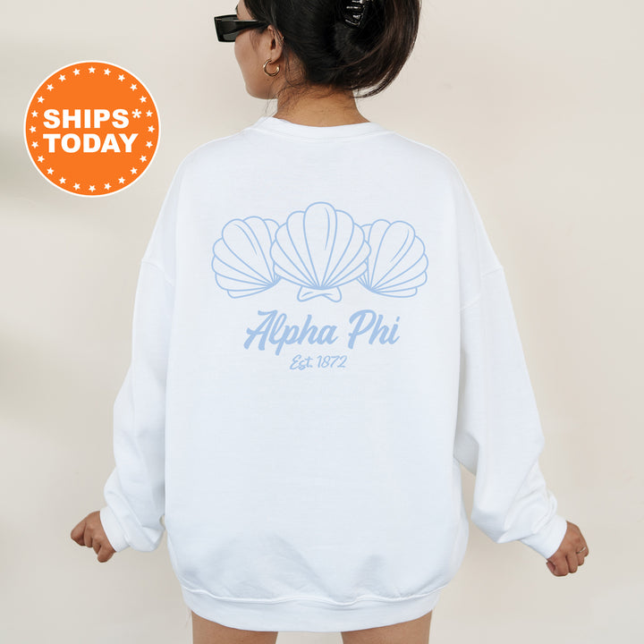 A person wearing a white sweatshirt with a graphic design of three shells and text that reads "Alpha Phi Est. 1872".