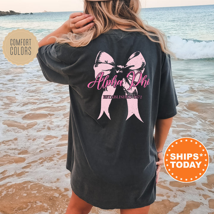 a woman standing on a beach wearing a black shirt with a pink ribbon